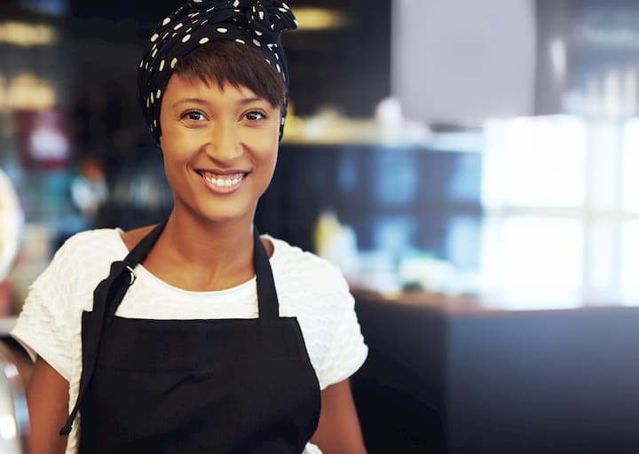 mulher negra dona do próprio negócio. Ao fundo, sua loja.